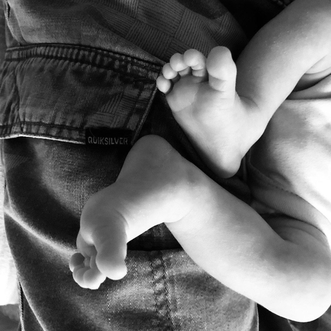 two small baby feet in black and white resting on a father's leg 